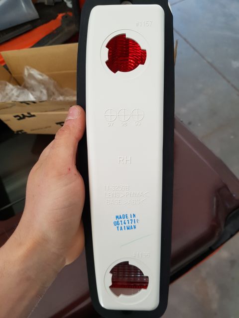 1978 Ford Bronco - A person's hand holds a white taillight assembly with red reflectors. The assembly has text indicating it is for the right-hand side and ma…