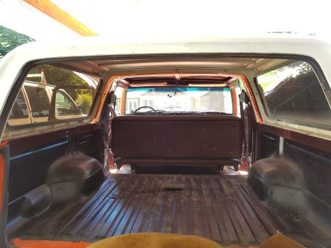 1978 Ford Bronco - View from the rear cargo area of a classic Ford Bronco, looking forward into the interior. The vehicle has a white roof and orange-painted…