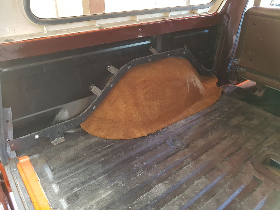 Interior cargo area of a classic SUV with brown carpeted wheel well and worn metal floor.