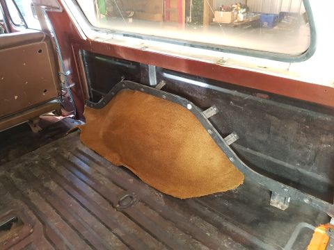 1978 Ford Bronco - The interior of a vehicle's cargo area shows a piece of brown carpet lining the side panel. The metal floor of the cargo area is visible, a…
