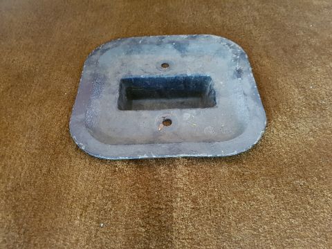 1978 Ford Bronco - A rectangular metal part with a raised rectangular opening in the center and two holes is shown on a brown textured surface. The part appea…