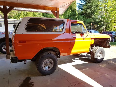 1978 Ford Bronco - The side view of an orange and white 1978 Ford Bronco is shown parked under a covered structure. The front of the vehicle is missing its fe…