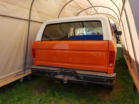 1978 Ford Bronco - The rear of an orange 1978 Ford Bronco is parked inside a portable garage. The vehicle has a white roof and a black bumper with a trailer h…