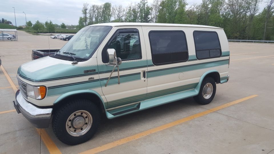 Cream and teal 1990s Ford E-350 van parked in a lot.