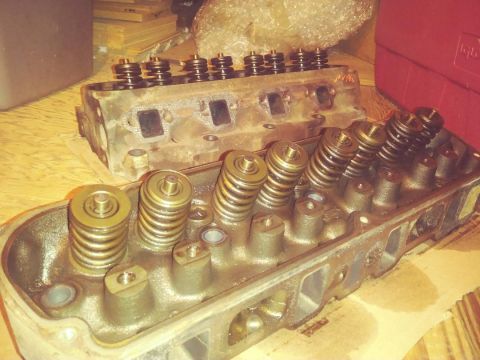 1996 Ford Bronco - Two cast iron cylinder heads with valve springs and retainers are shown. The head in the foreground is angled towards the viewer, while the…