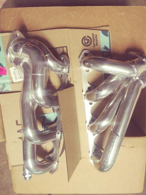 1996 Ford Bronco - Two polished stainless steel exhaust headers are laid out on top of cardboard boxes. The header on the right has a logo that appears to say…