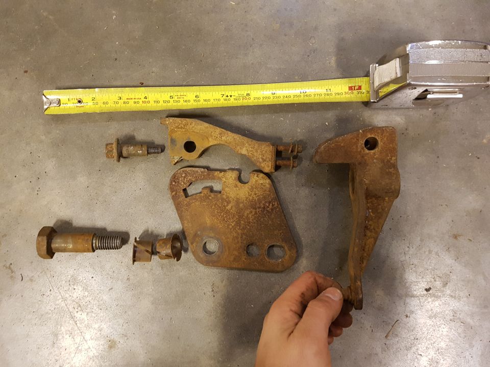 Rusty metal brackets and bolts on concrete floor with measuring tape.