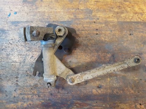 1978 Ford Bronco - A rusty metal linkage assembly with a lever arm is mounted on a wooden surface. The assembly appears to be a mechanical component from a ve…