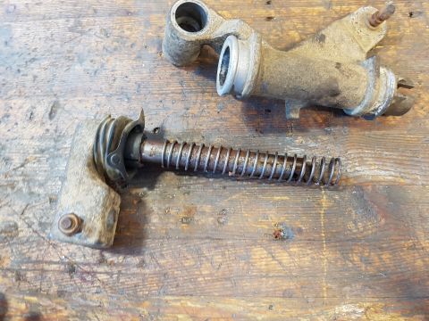 1978 Ford Bronco - Two disassembled metal parts, likely from a vehicle's braking or clutch system, rest on a weathered wooden surface. One part features a coi…