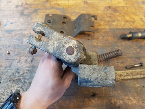 1978 Ford Bronco - A person's hand holds a rusty metal mechanical part with a spring attached, resting on a wooden workbench.