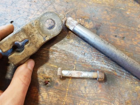 1978 Ford Bronco - A person's hand is holding a rusty metal bracket on a wooden surface. A bolt and a metal rod are also visible on the surface.