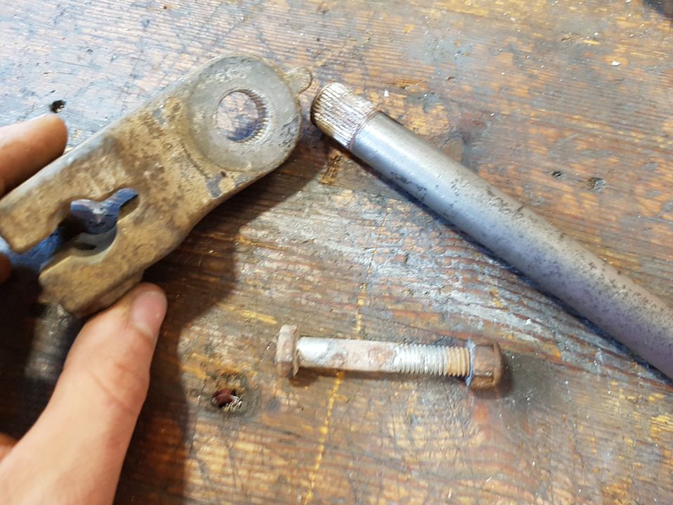 Rusty metal bracket, bolt, and rod on a wooden surface.