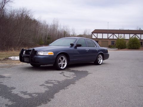2001 Ford Crown Victoria - A dark blue Ford Crown Victoria, possibly a police car, is parked in front of a building with a distinctive architectural style.