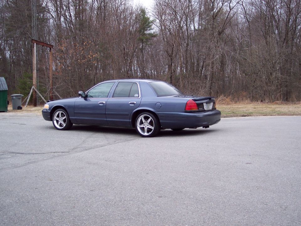 Dark blue Ford Crown Victoria sedan rear three-quarter with chrome wheels and black trunk spoiler