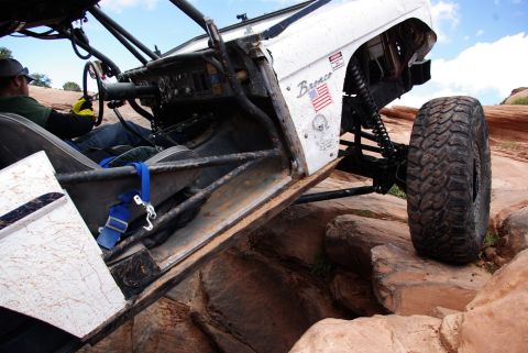 1995 Ford Bronco - A heavily modified white Ford Bronco is navigating a rocky, off-road trail. The driver, wearing a hat and yellow gloves, is visible behind…