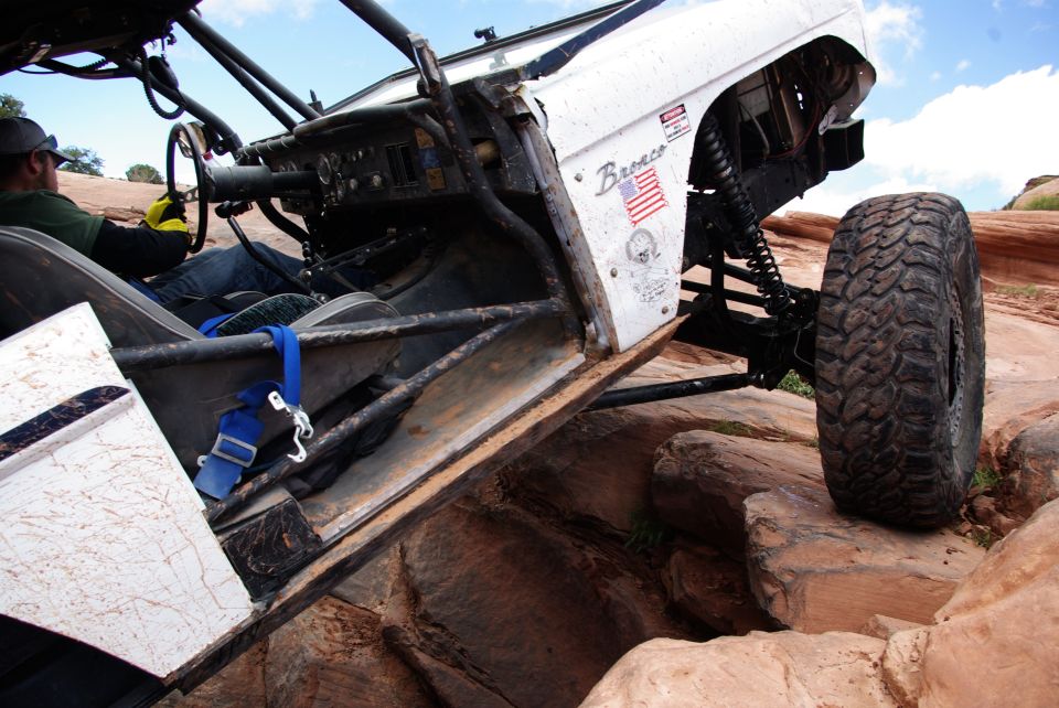 Modified white Ford Bronco on a rocky trail, driver visible inside.