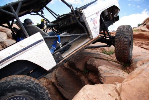 1995 Ford Bronco - A white Ford Bronco is navigating a rocky, off-road trail, with its front tire angled upwards on a large boulder. The vehicle features a ro…