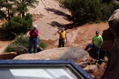 1995 Ford Bronco - Three people are posing for photos in a rocky, desert landscape with sparse vegetation. The person on the left is wearing a magenta shirt a…
