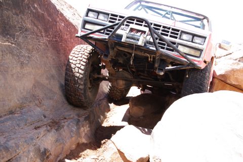 1995 Ford Bronco - A red off-road vehicle navigates a narrow canyon with large tires on rocky terrain. The vehicle's front end, including the bumper and grill…