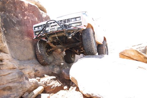 1995 Ford Bronco - A lifted, off-road modified pickup truck navigates a rocky, desert-like terrain, with its front tires climbing over a large boulder. The ve…