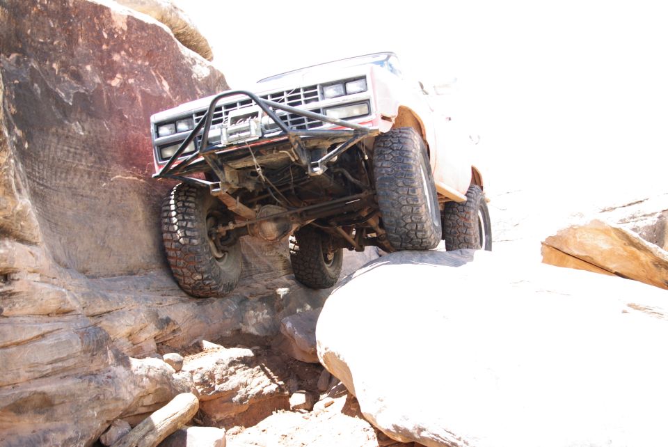 Lifted pickup truck with off-road tires climbing a rock obstacle