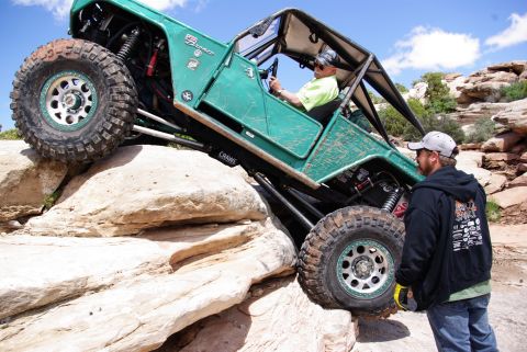 1995 Ford Bronco - A heavily modified green Ford Bronco is navigating a steep, rocky incline with a person in the driver's seat and another person standing ne…