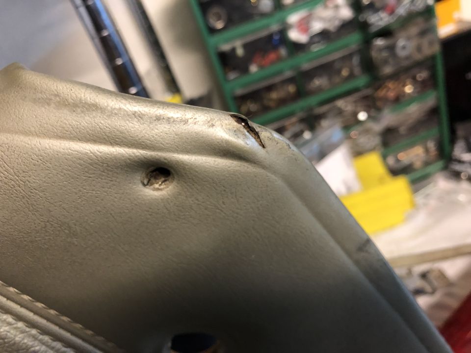 Damaged gray interior trim piece with a hole and a tear.