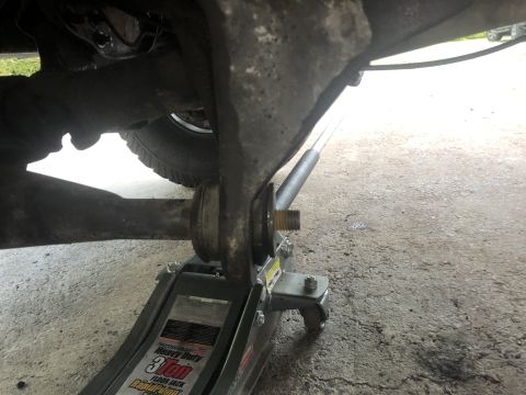 1995 Ford Bronco - A floor jack is supporting the suspension of a vehicle, with a tire visible in the background. The jack is positioned under a suspension co…