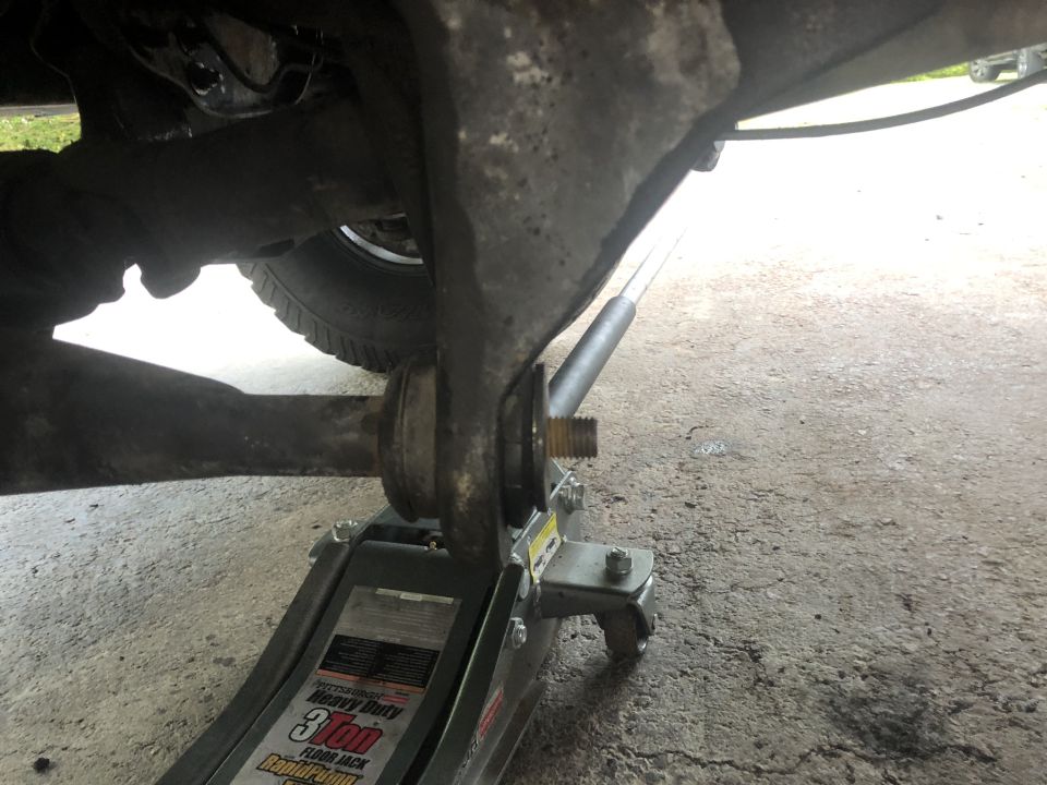Floor jack supporting vehicle suspension, tire visible.