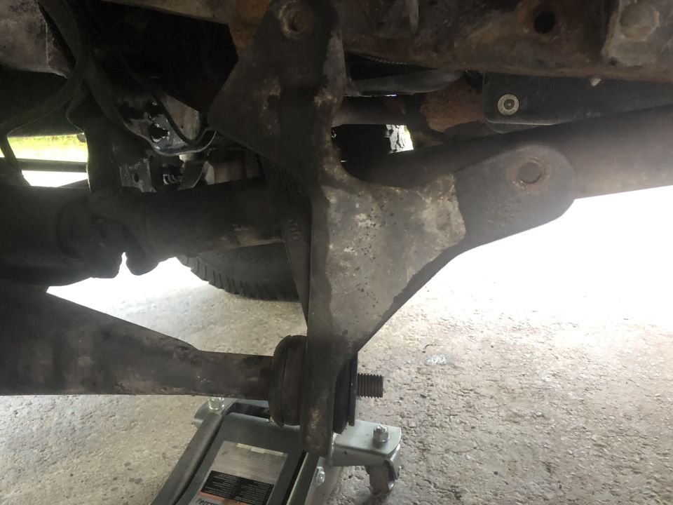 Underside of a vehicle showing a suspension part supported by a jack.