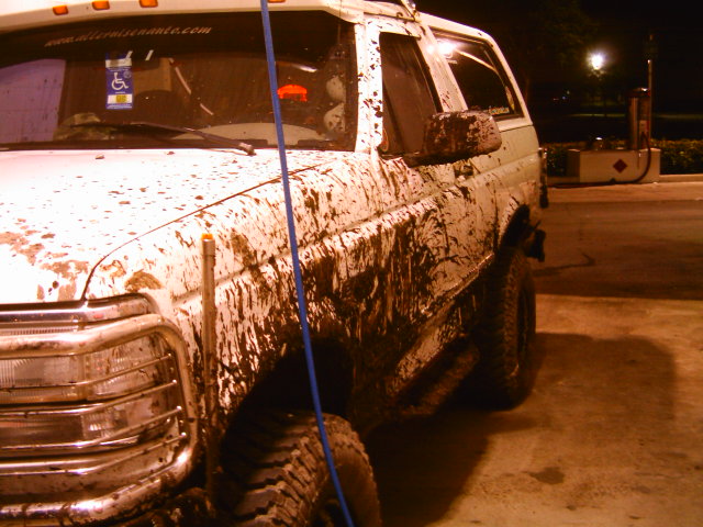 Mud-covered white 1995 Ford Bronco parked at a gas station at night.