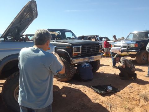 1985 Ford Bronco - A person stands near a lifted truck with its hood open under a clear blue sky.