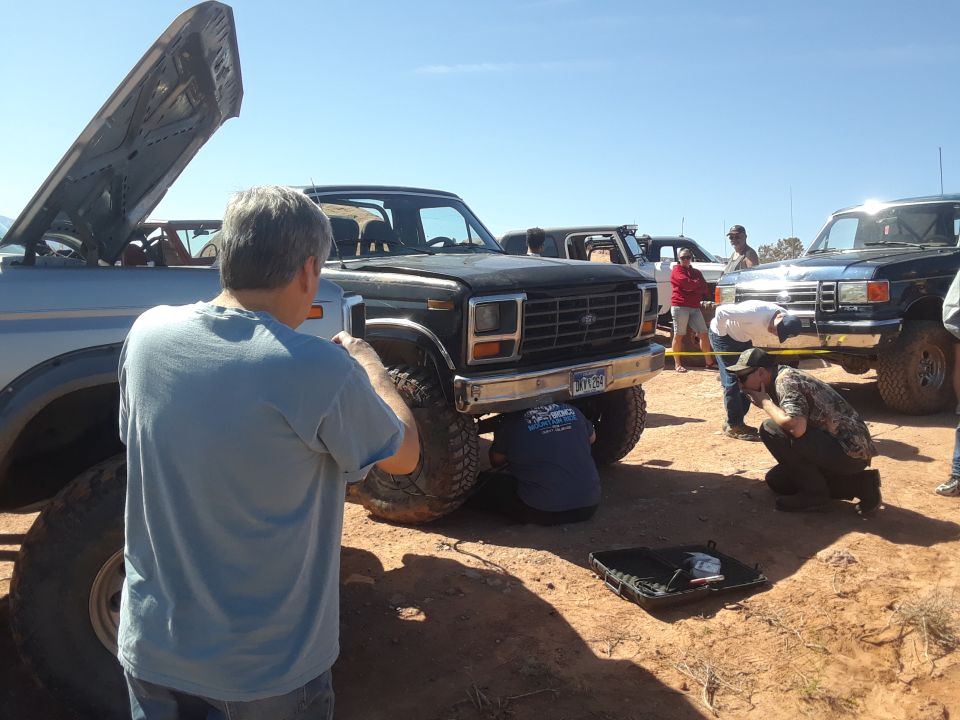 Lifted truck with hood open, person in foreground, sunny day, dirt ground