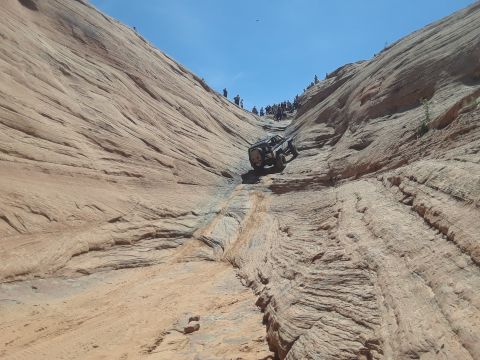1985 Ford Bronco - A vehicle navigates a tight passage between towering sandstone cliffs under a clear blue sky.