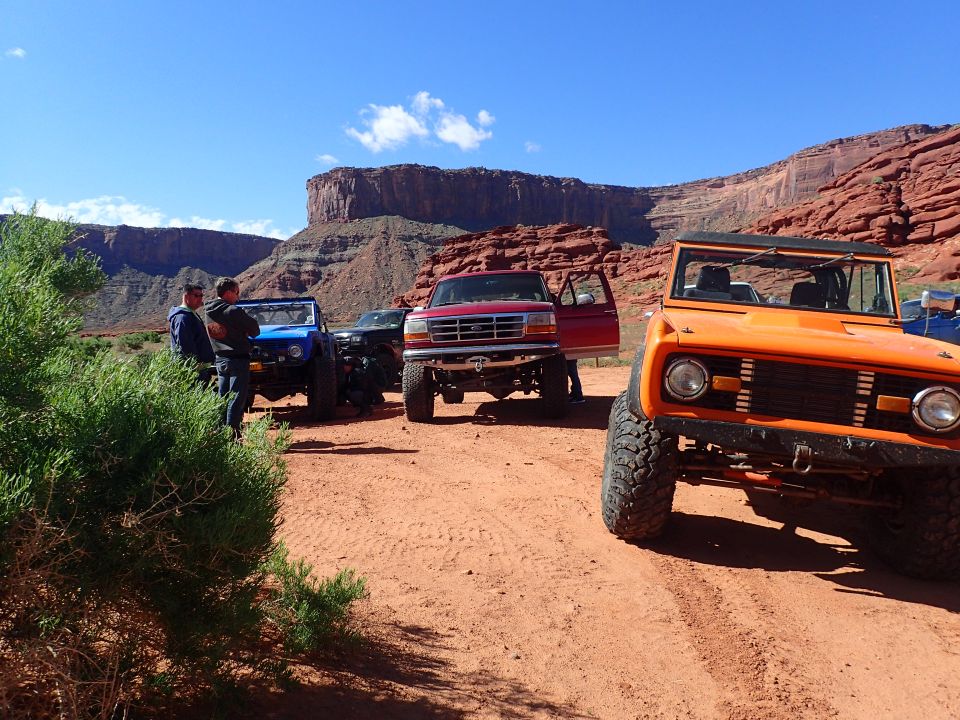 Orange SUV with large tires parked on a dirt road with red rock cliffs in the background.
