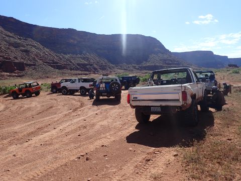 1995 Ford Bronco - Several off-road vehicles are parked on a dirt road in a canyon landscape. A white Ford Bronco with its top removed is in the foreground, w…