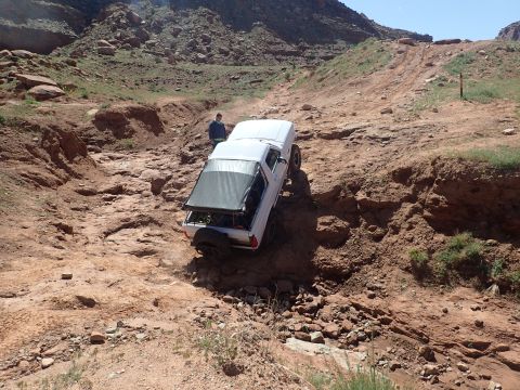 1995 Ford Bronco - A white 1995 Ford Bronco is navigating a steep, rocky, off-road trail with a person standing nearby. The vehicle is tilted at an angle as i…