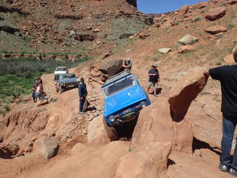 1995 Ford Bronco - A blue off-road vehicle navigates a rocky, steep trail with several other vehicles and people in the background.