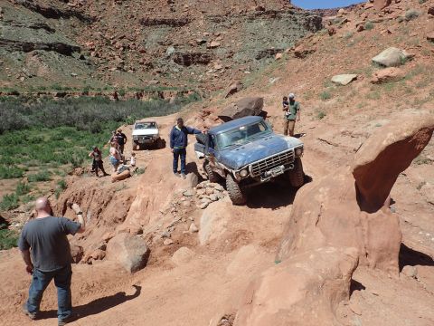 1995 Ford Bronco - A blue Ford pickup truck navigates a rocky, off-road trail with several people watching and standing nearby. The truck is positioned on a s…
