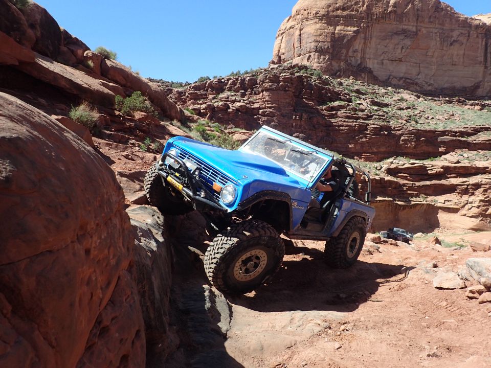 Blue Ford Bronco off-roading on a steep, rocky trail.