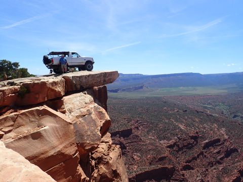 1995 Ford Bronco - A man stands next to a white Ford Bronco parked on the edge of a large rock formation overlooking a vast canyon landscape under a clear blu…