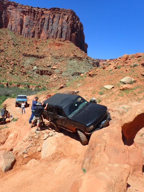 1995 Ford Bronco - A black Ford Bronco is navigating a rocky, off-road trail with several people assisting. The vehicle is angled on a steep incline, with its…