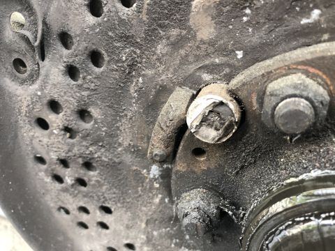 1995 Ford Bronco - A close-up view shows a heavily greased and dirty brake rotor with several holes. A damaged bolt head is visible in the center of the frame…