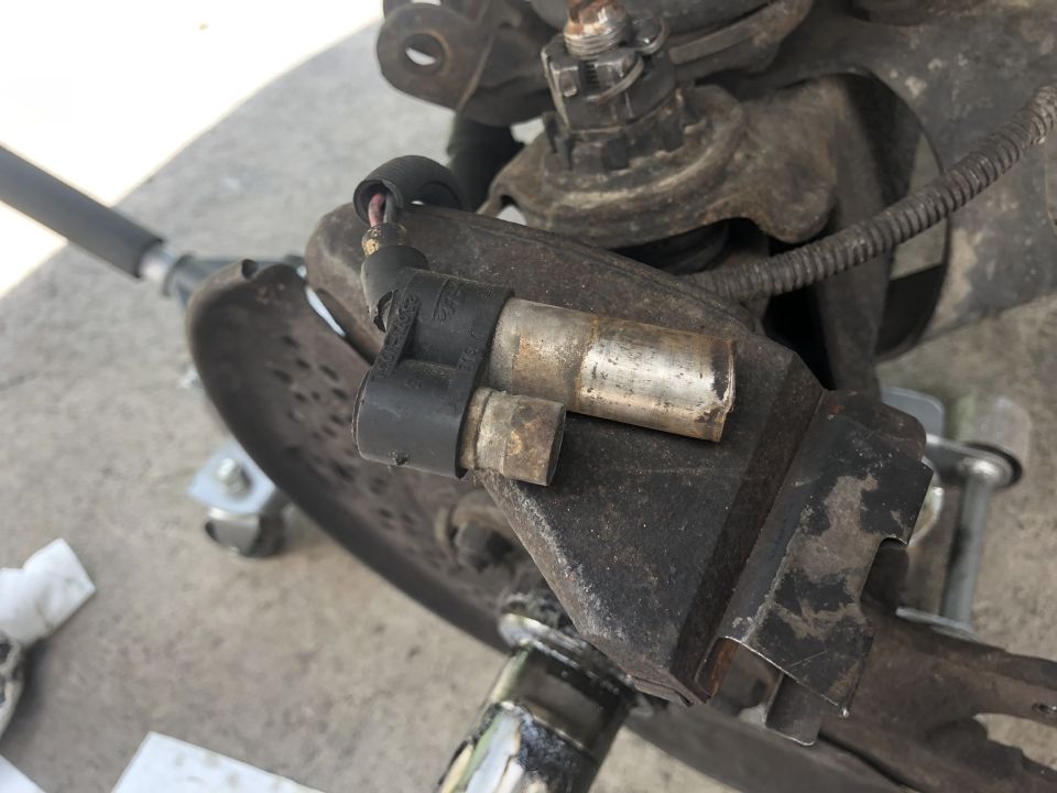 Disassembled axle or steering component showing solenoid-style actuator and cast bracket