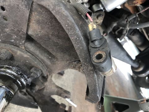 1995 Ford Bronco - A close-up view of a vehicle's ABS speed sensor mounted to the suspension near the wheel hub. The sensor is black with a gold connector and…