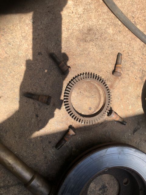 1995 Ford Bronco - Several rusty lug nuts and a toothed metal ring are scattered on a concrete surface next to a brake rotor. A shadow of a person is cast acr…