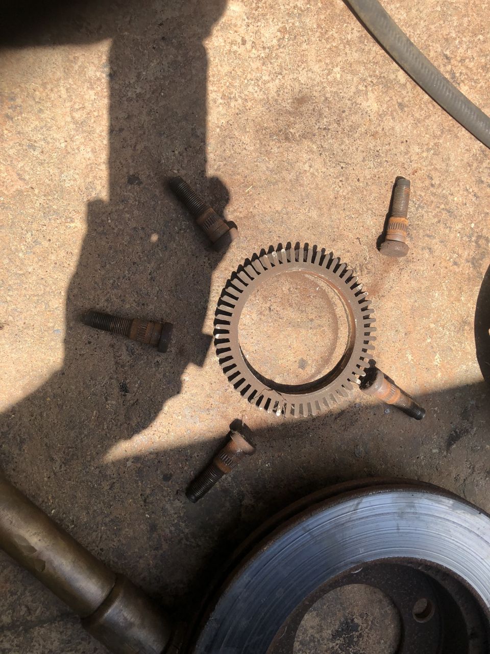 Rusty lug nuts and a toothed metal ring on concrete near a brake rotor.