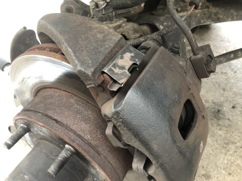 1995 Ford Bronco - A close-up view of a rusty brake caliper and rotor assembly on a vehicle. The brake caliper is black and shows signs of wear, while the rot…