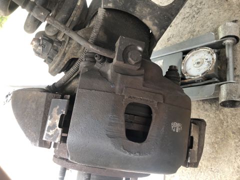 1995 Ford Bronco - A close-up view of a vehicle's brake caliper and rotor assembly, showing some rust and wear. A hydraulic car jack is visible in the backgro…