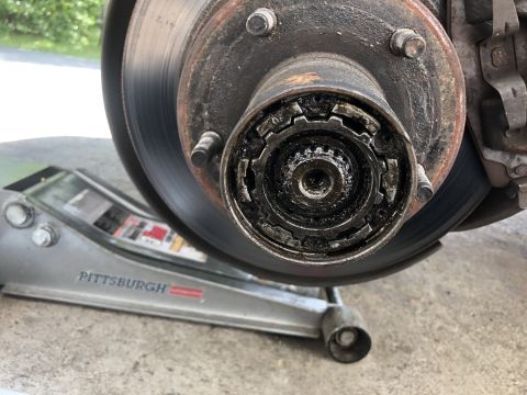 1995 Ford Bronco - A close-up view of a vehicle's front wheel hub assembly, showing a manual locking hub mechanism covered in grease. A silver hydraulic floor…